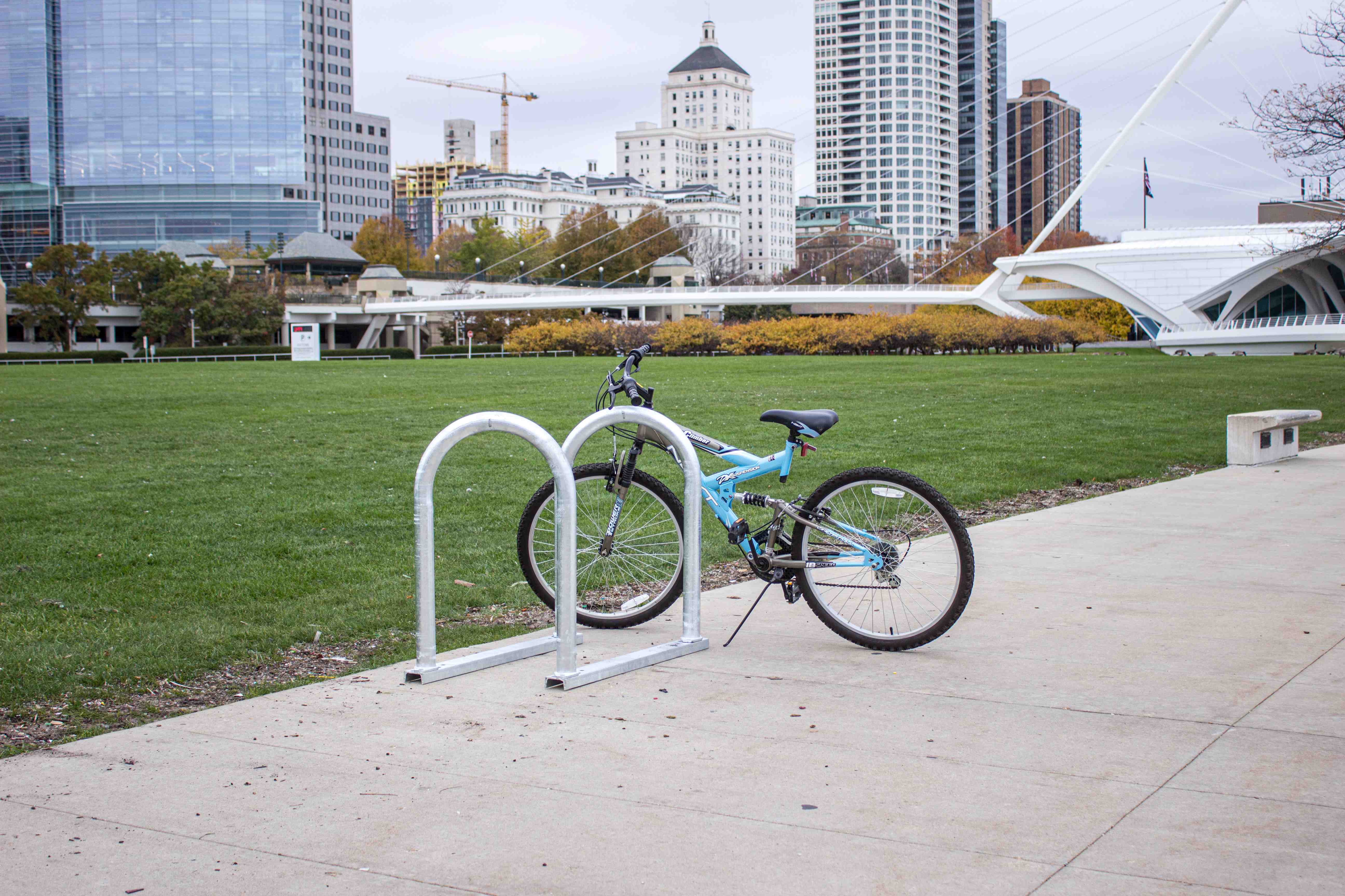 A bike is securely parked on a bike rack in a green park setting, surrounded by trees and open space.