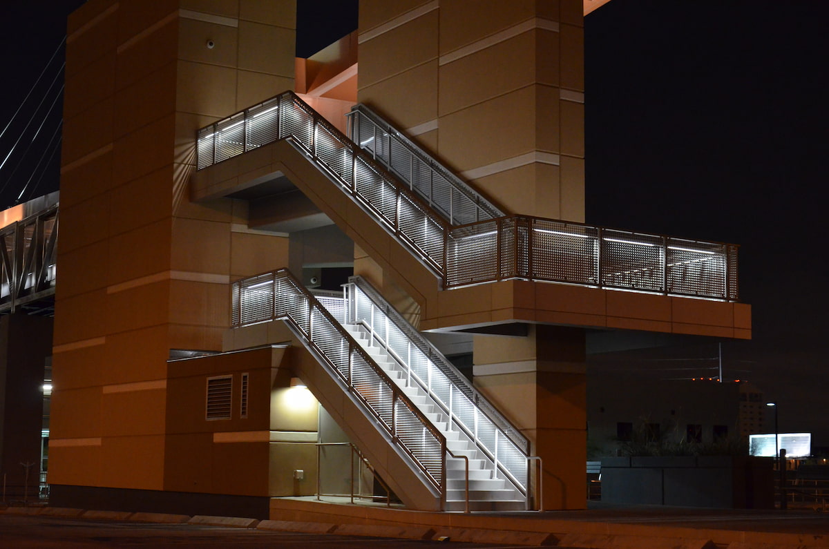 Nighttime view of illuminated zigzag metal staircases outside a modern brown building, creating a striking, industrial urban scene.