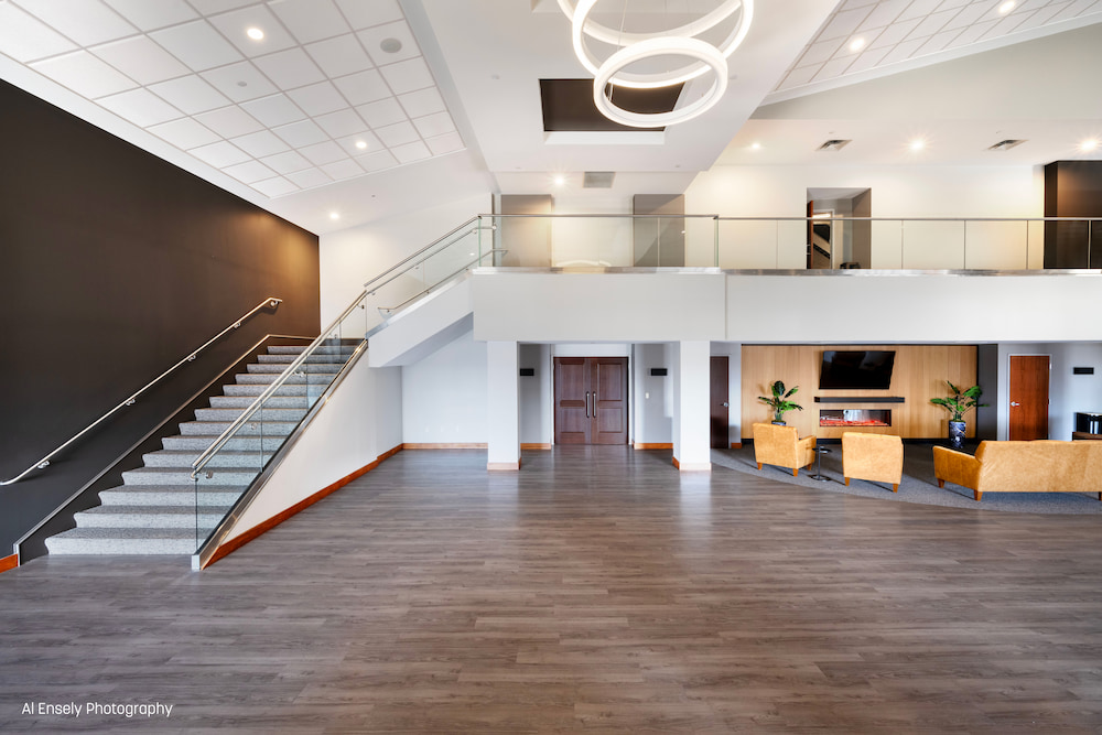 Modern lobby with gray floor, glass staircase, circular ceiling lights, and seating area with tan chairs.