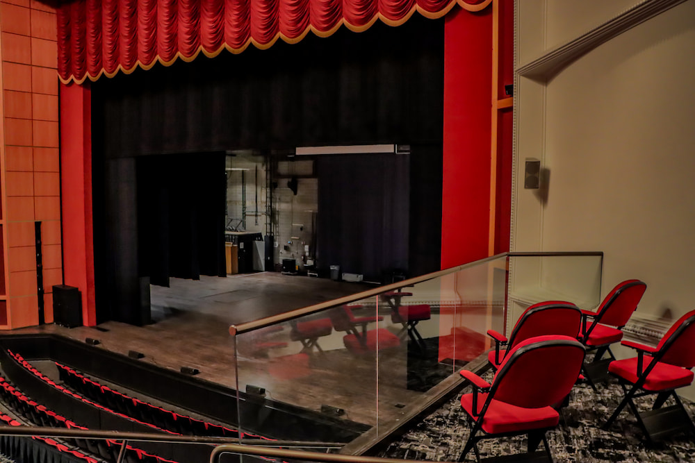 View of theater stage with red curtains and a prominent glass railing.