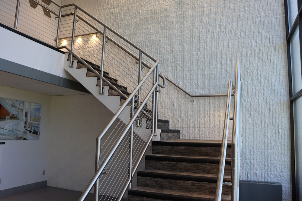 Indoor staircase with metal railings and cable design against a textured wall.